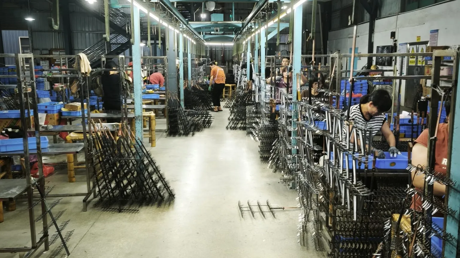 Electroplating racks loaded with metal parts lining a long factory aisle, with operators at their benches